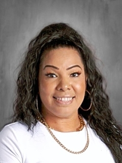 Smiling woman with long curly hair, wearing a white top and gold jewelry, against a gray background.