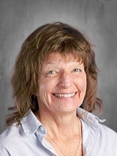 A woman with shoulder-length hair smiles at the camera, wearing a light collared shirt against a neutral background.