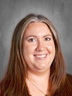 Smiling person with long brown hair against a gray background.