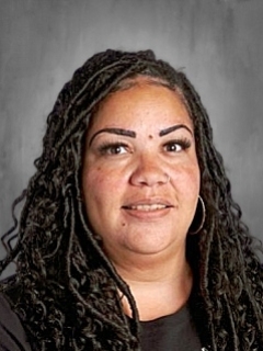 Person with long curly hair and hoop earrings, smiling against a gray background.