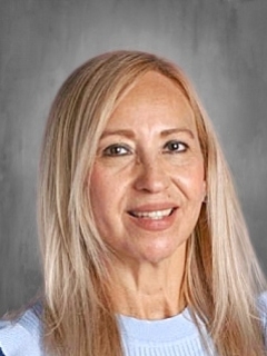 A person with long blonde hair smiles against a gray background, wearing a light blue top.